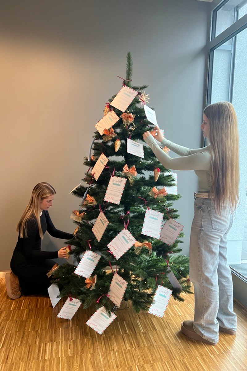 Zwei Frauen schmücken den Weihnachtsbaum mit den ausgefüllten Wunschzetteln des Seniorenheims.