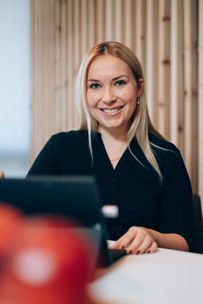 Eine lächelnde junge Frau sitzt an einem Laptop.