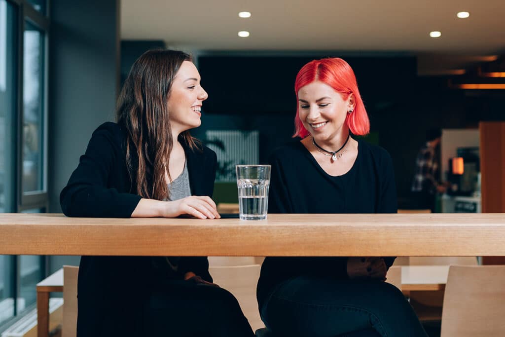 Zwei junge Frauen sitzen fröhlich an einem Tisch.