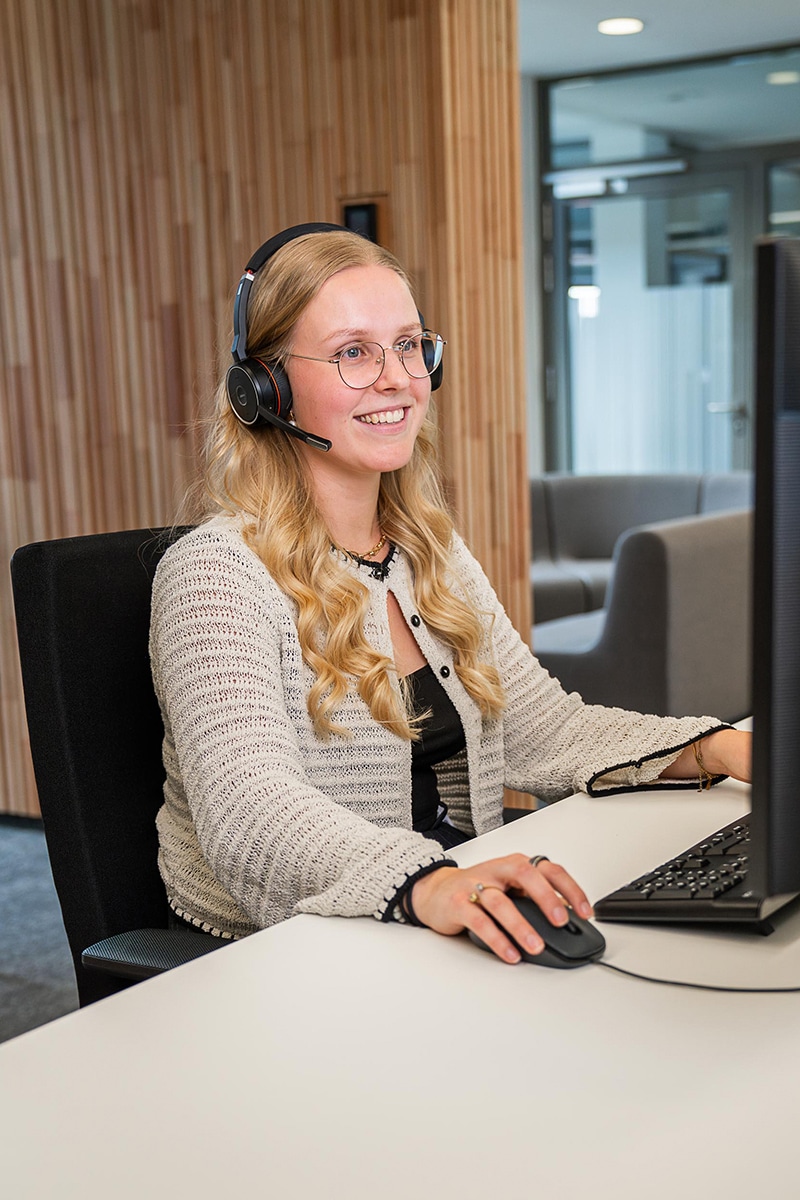 Eine junge Frau mit blonden Haaren und Headphone sitzt an einem PC.