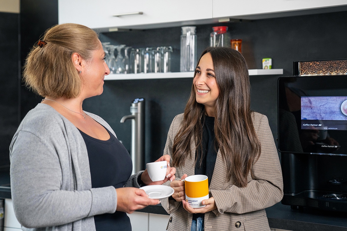 Zwei Kolleginnen unterhalten sich an der Kaffeemaschine.